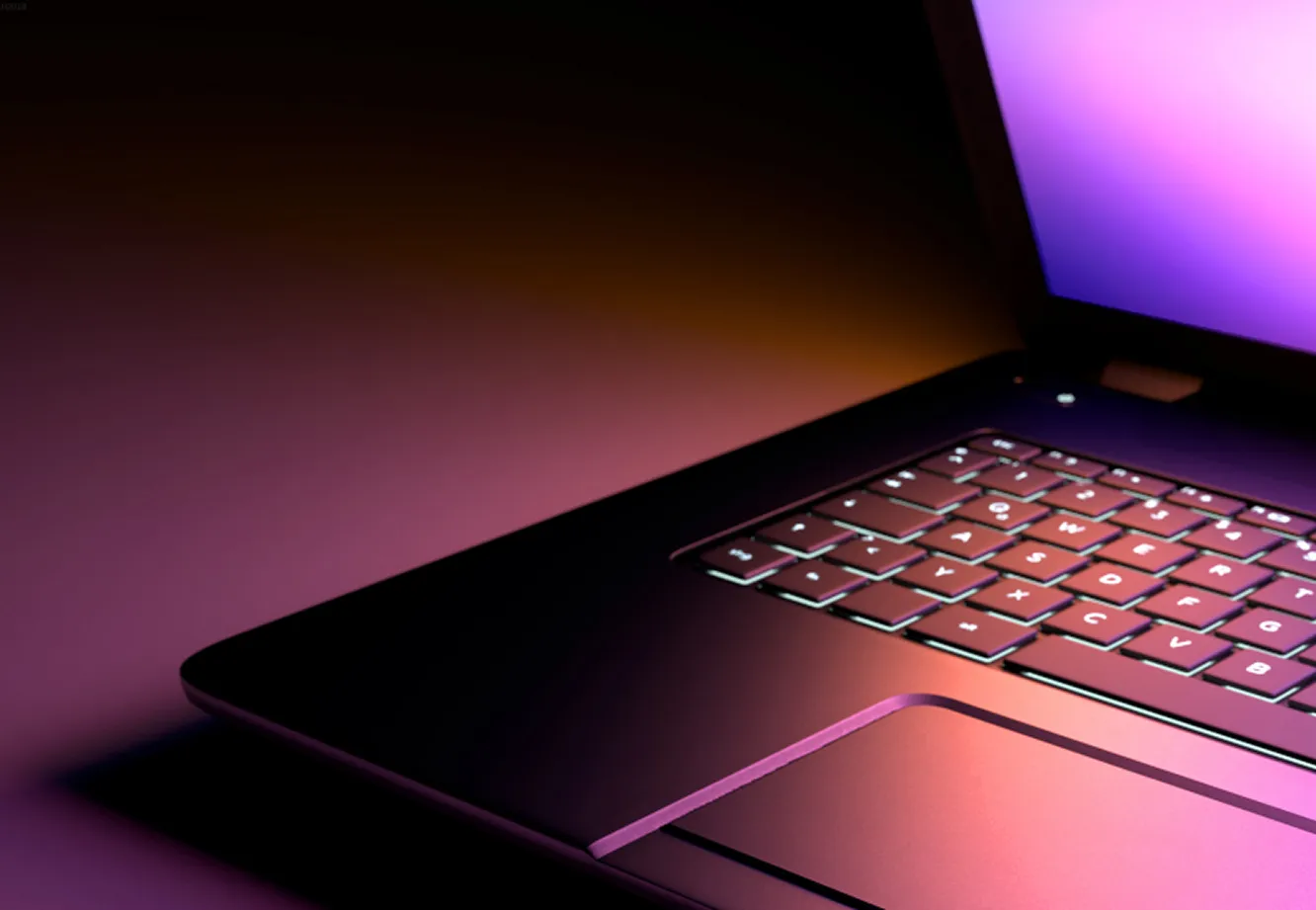 Close-up de um notebook aberto com teclado iluminado em tons de laranja e roxo